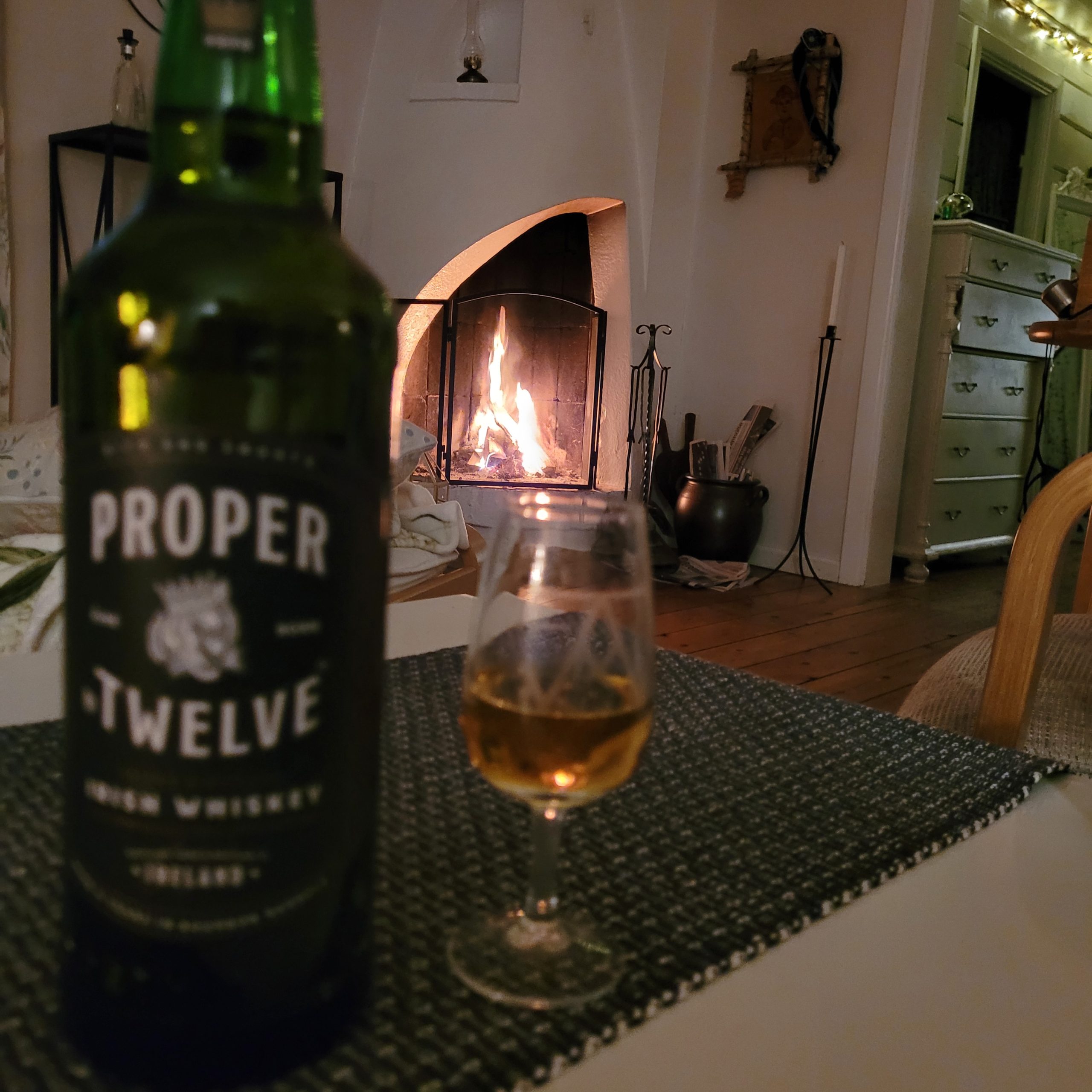 Proper No. Twelve Irish whiskey i glas framför öppen brasa
